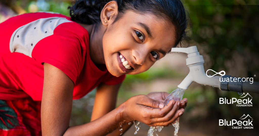 Young girl collecting clean water from a spout, smiling at the camera.