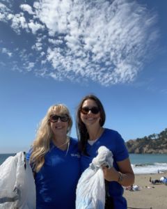 Two women smiling, holding bags of trash they collected